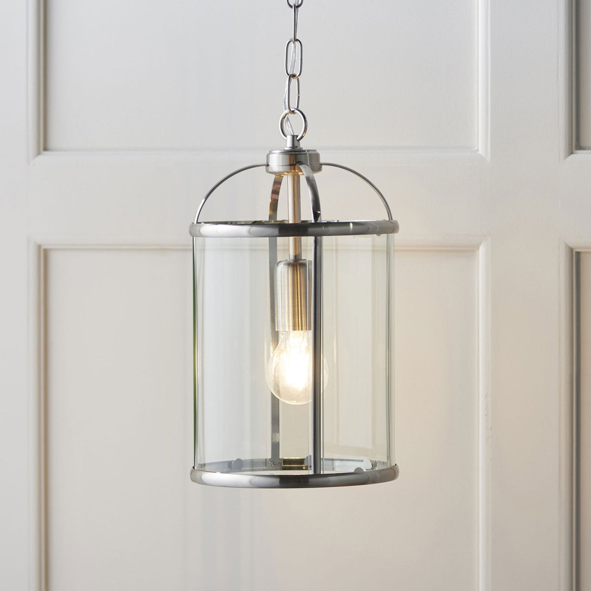 Caged ceiling light with a clear glass shade and a brushed steel finish, hanging against a white paneled wall.