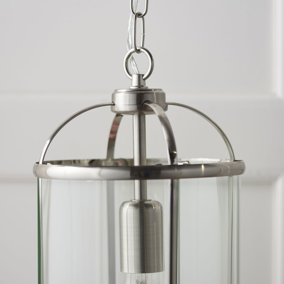 Close-up of the top of a caged ceiling light, showing the brushed steel frame and chain against a white wall.
