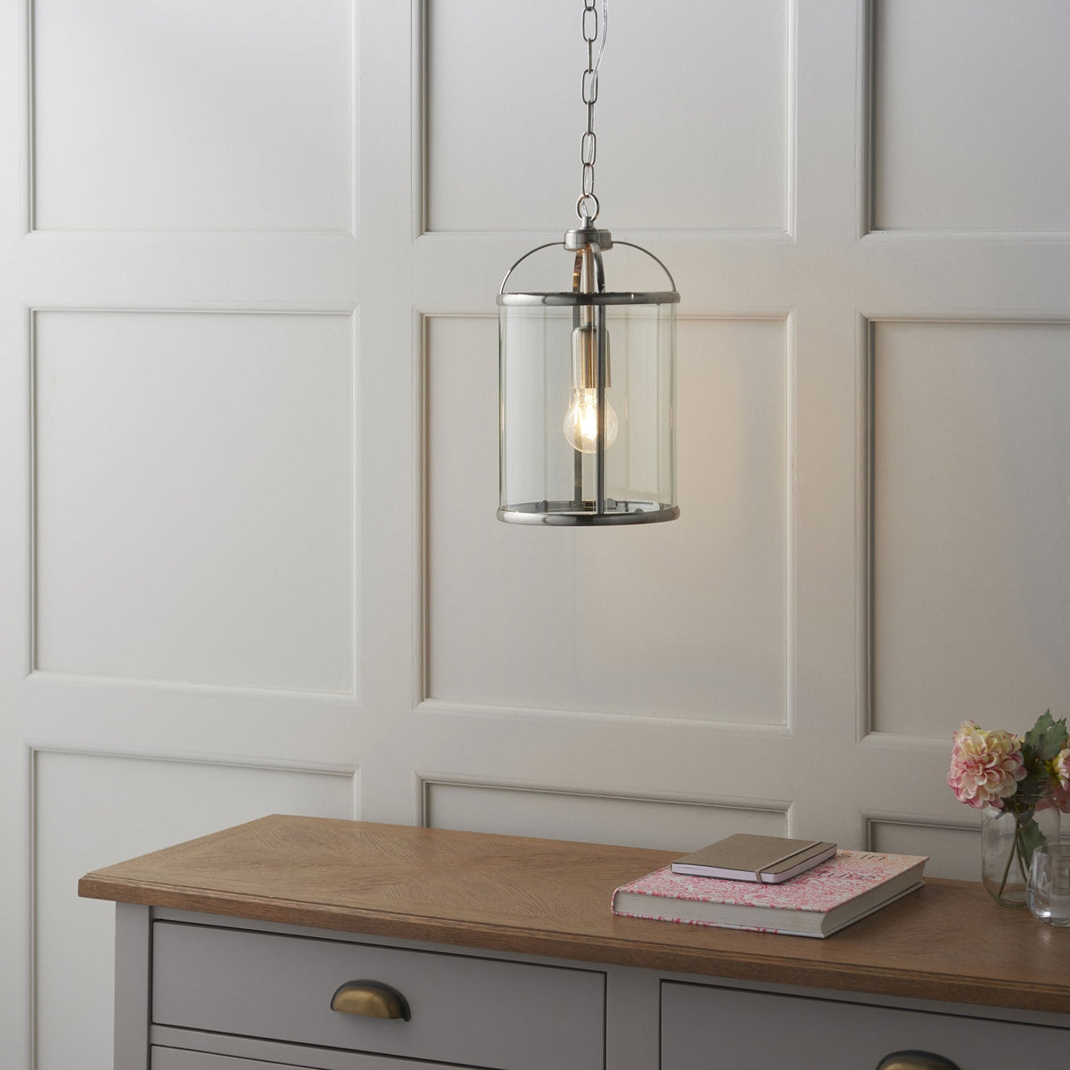 Caged ceiling light with a clear glass shade and a brushed steel finish, hanging above a grey wooden dresser.