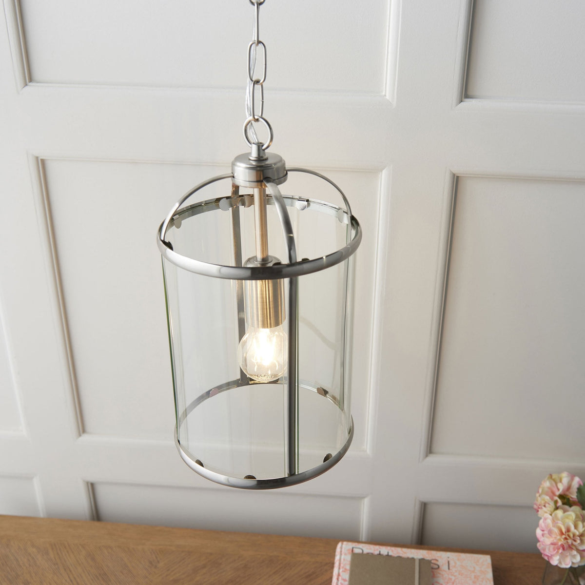 Overhead view of a caged ceiling light with a clear glass shade and a brushed steel finish, above a wooden surface.