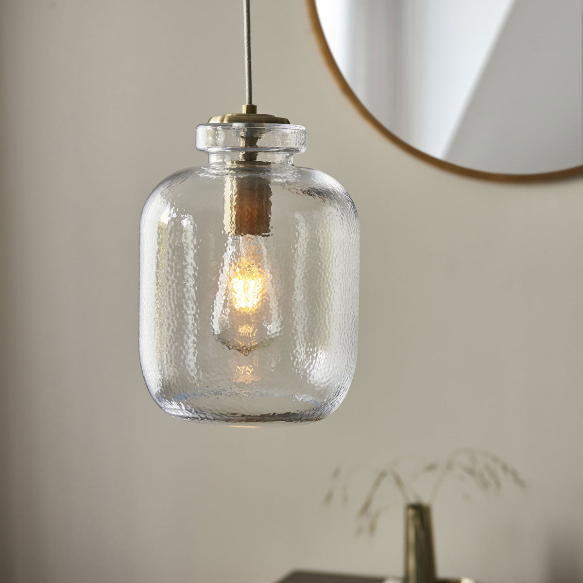 A clear, hammered glass pendant light with a brass top and visible filament bulb.