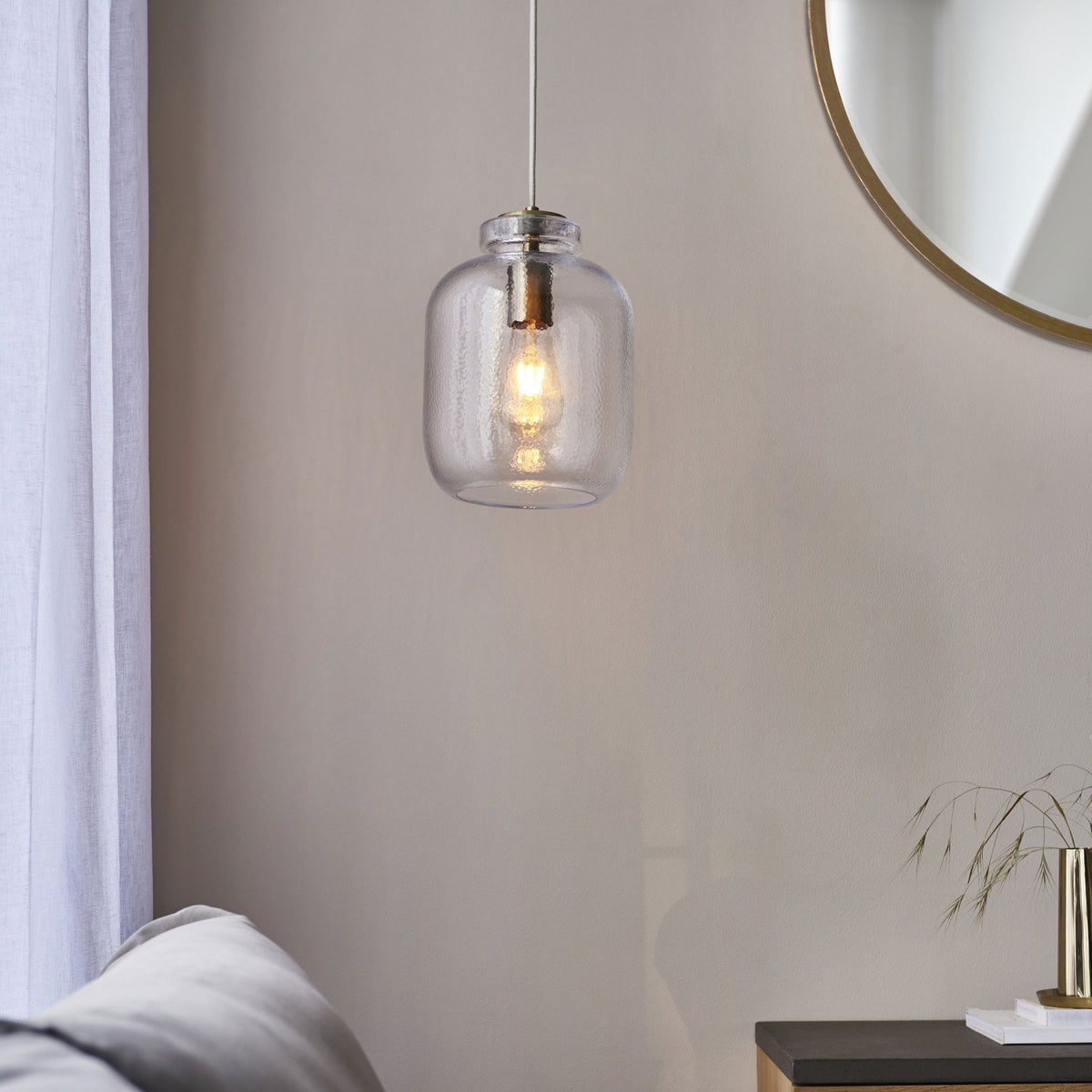 A clear glass pendant light illuminating a neutral living space with a round mirror.