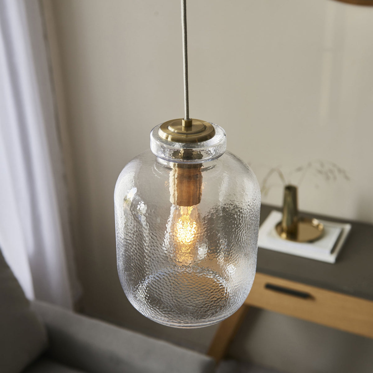 A close-up of a hammered glass pendant light with a brass fitting above a console table.