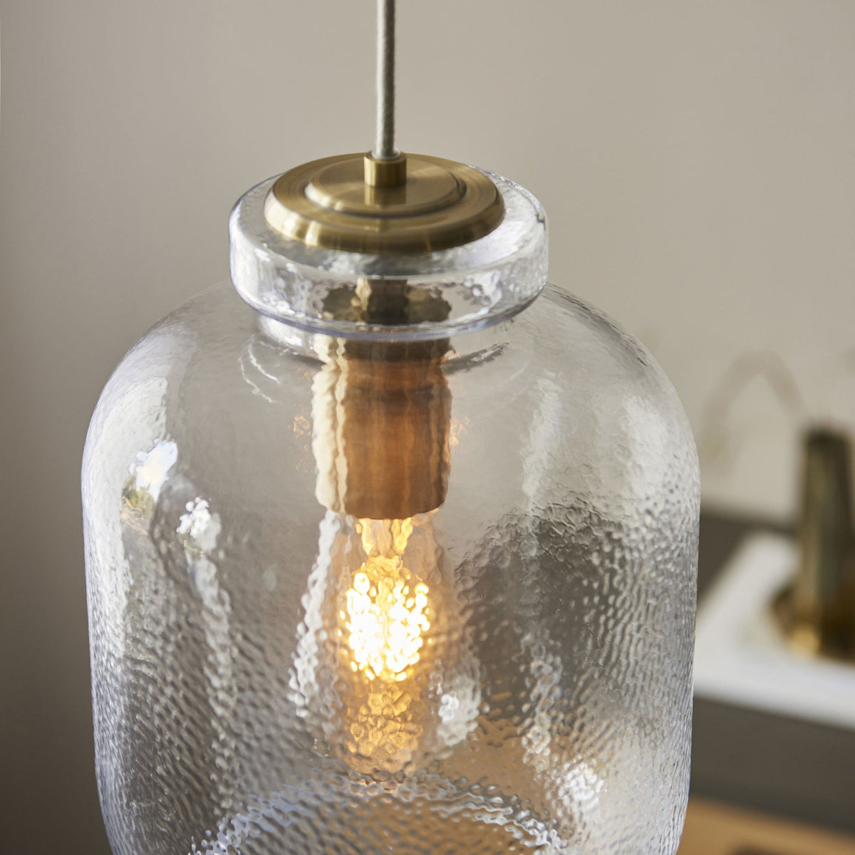 A close-up of the antique brass top and hammered glass of a lit pendant light.