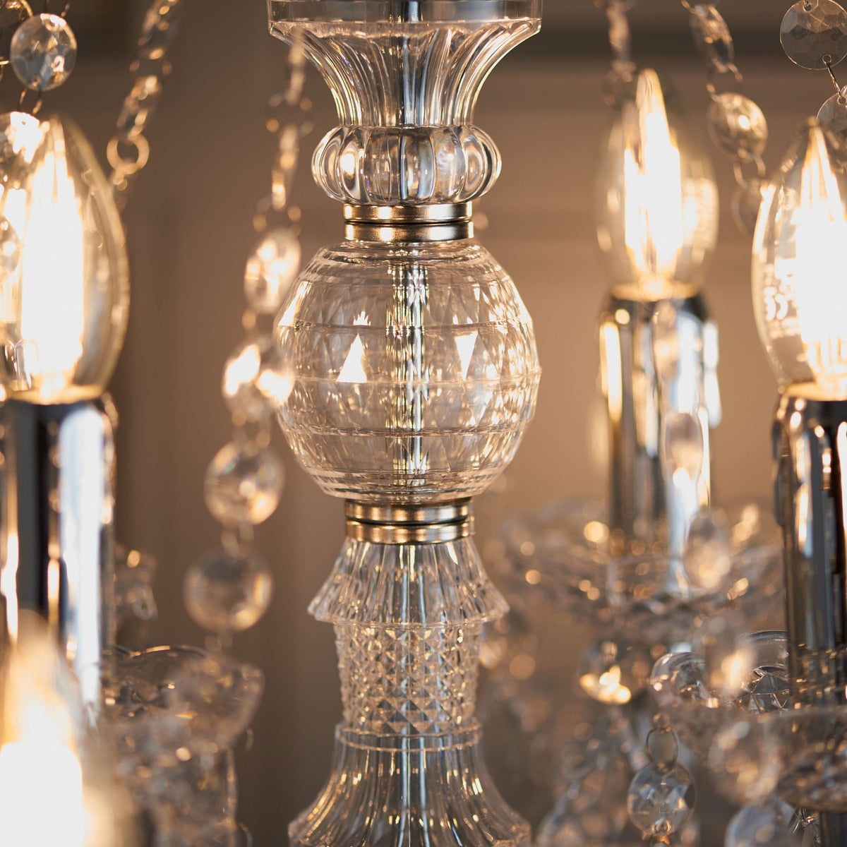 Detailed view of a crystal chandelier's central column with faceted glass and illuminated bulbs.