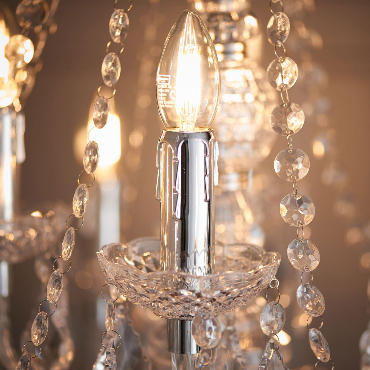 Close-up of a lit candle-style bulb on a crystal chandelier, surrounded by sparkling crystal strands.