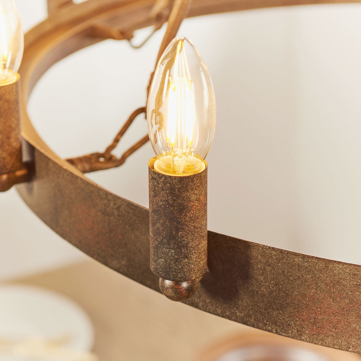 Detailed view of one illuminated candle-style bulb on the rustic bronze chandelier, highlighting its texture.