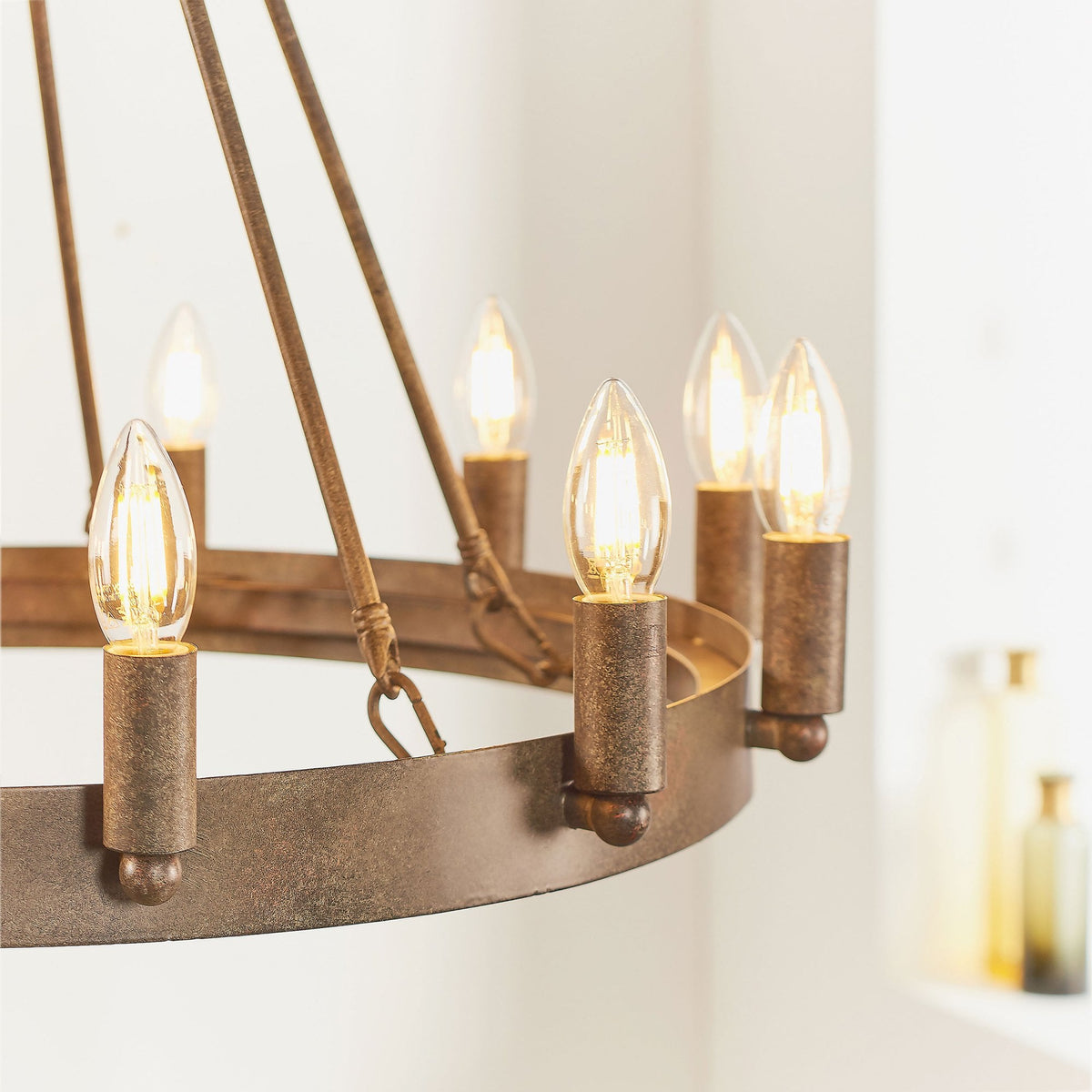 Side view of the rustic bronze chandelier with several illuminated candle-style bulbs against a bright background.