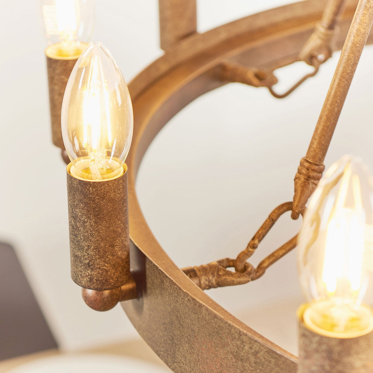 Close-up of an illuminated candle-style bulb on the rustic bronze chandelier, showing the textured metal ring.