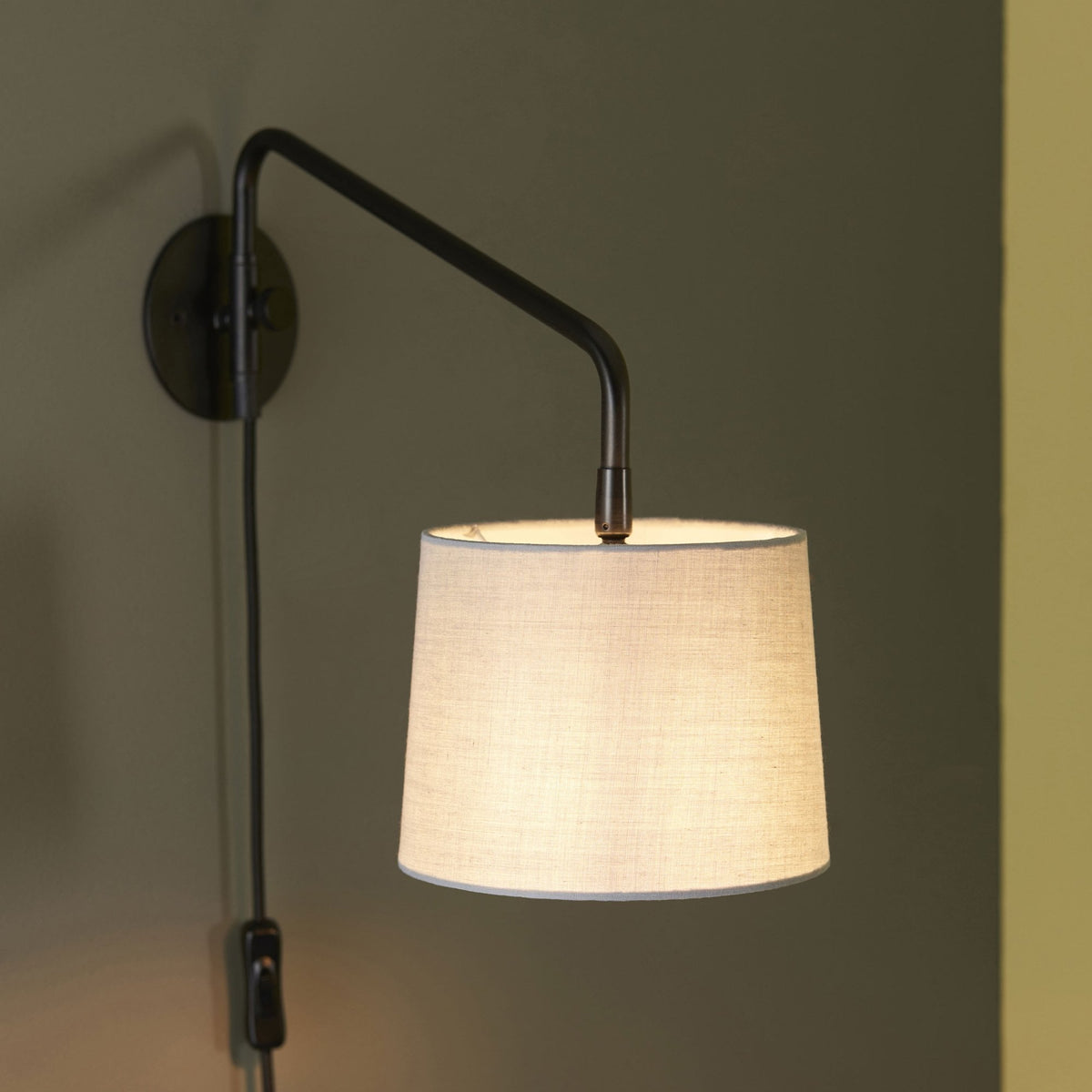 Close-up of a black wall light with a white fabric shade, casting a warm glow.