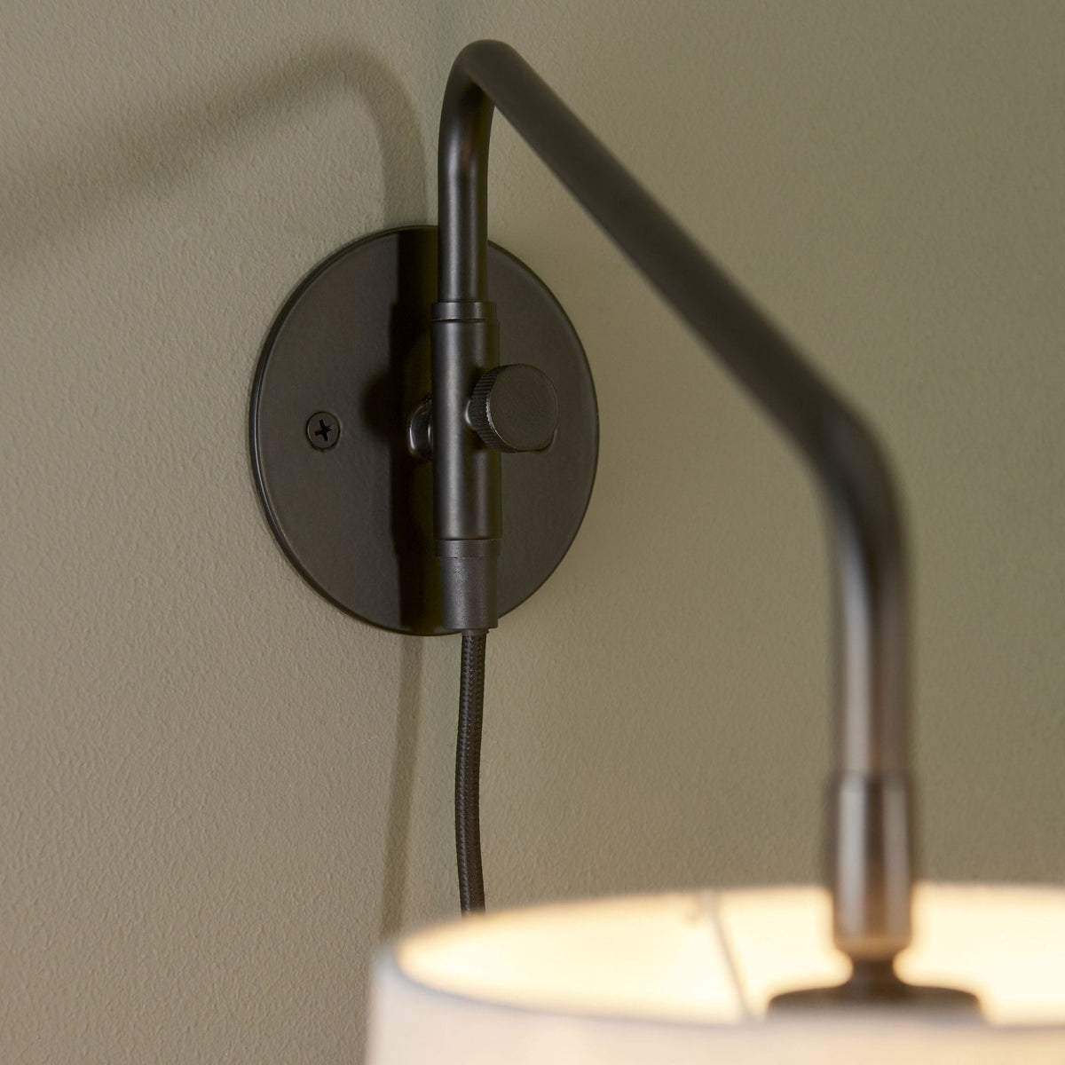 Detail of the black wall mount and adjustable arm of the wall light.