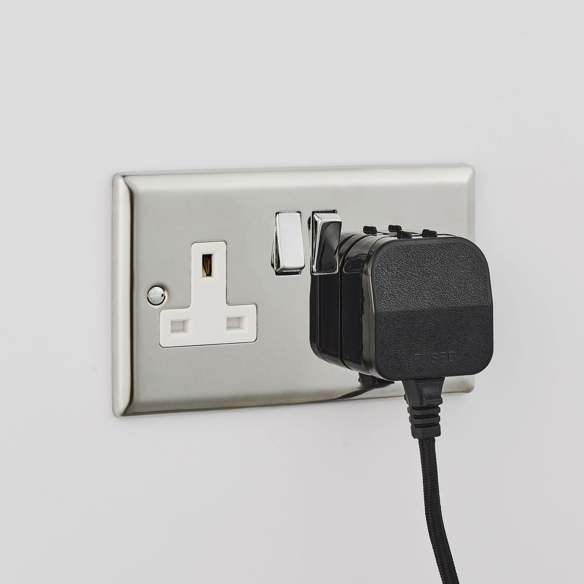 A black UK plug inserted into a silver wall socket with the switch in the 'on' position.