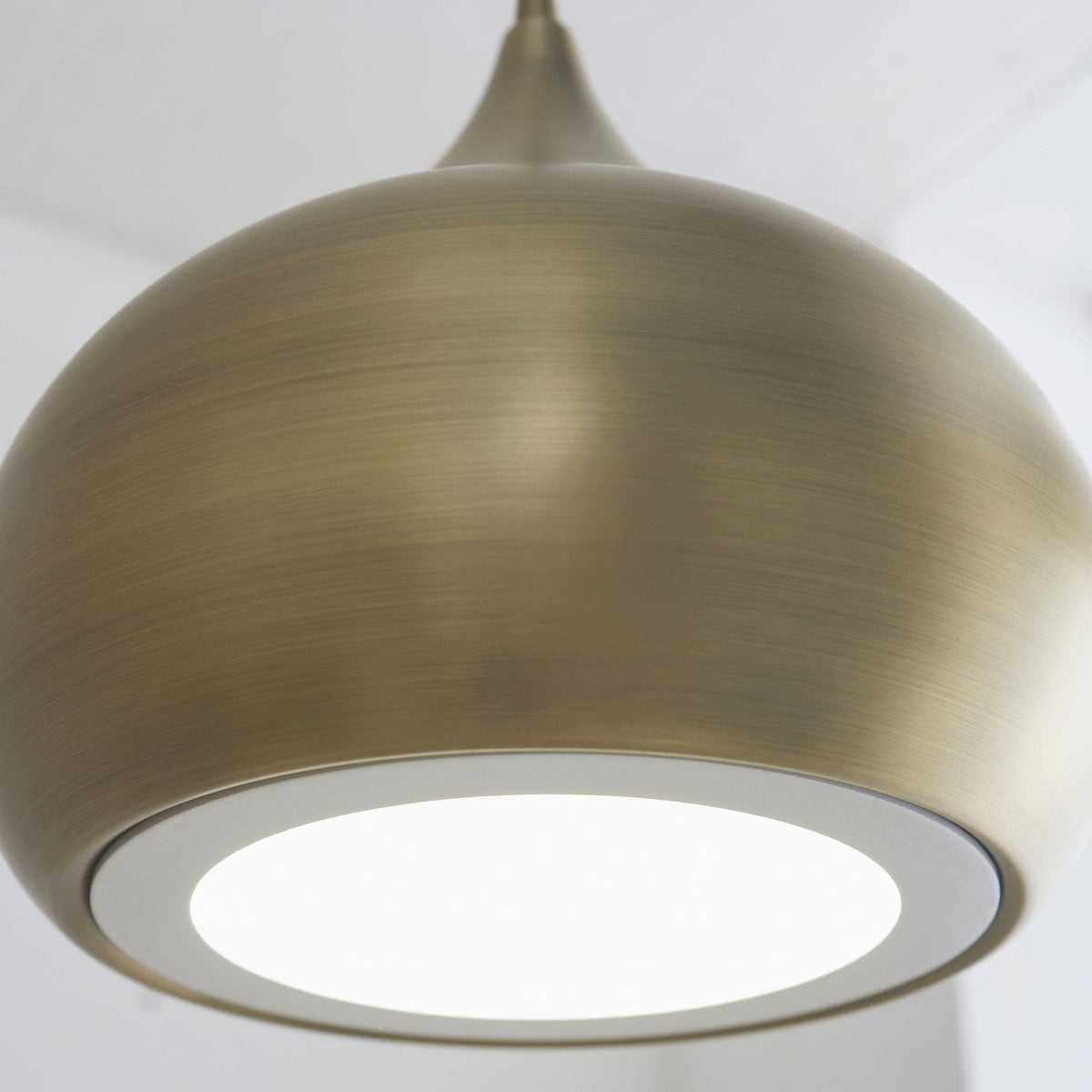 Close-up of the illuminated base of a brass pendant light, showing the white diffuser.