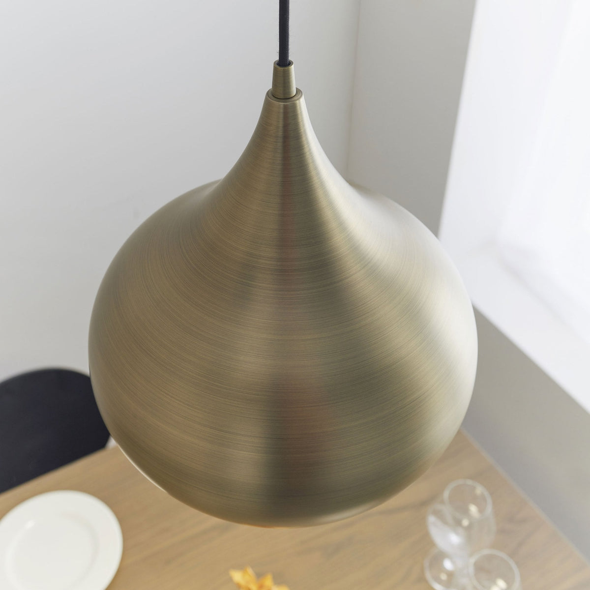 Overhead view of a brass pendant light hanging above a dining table with place settings.