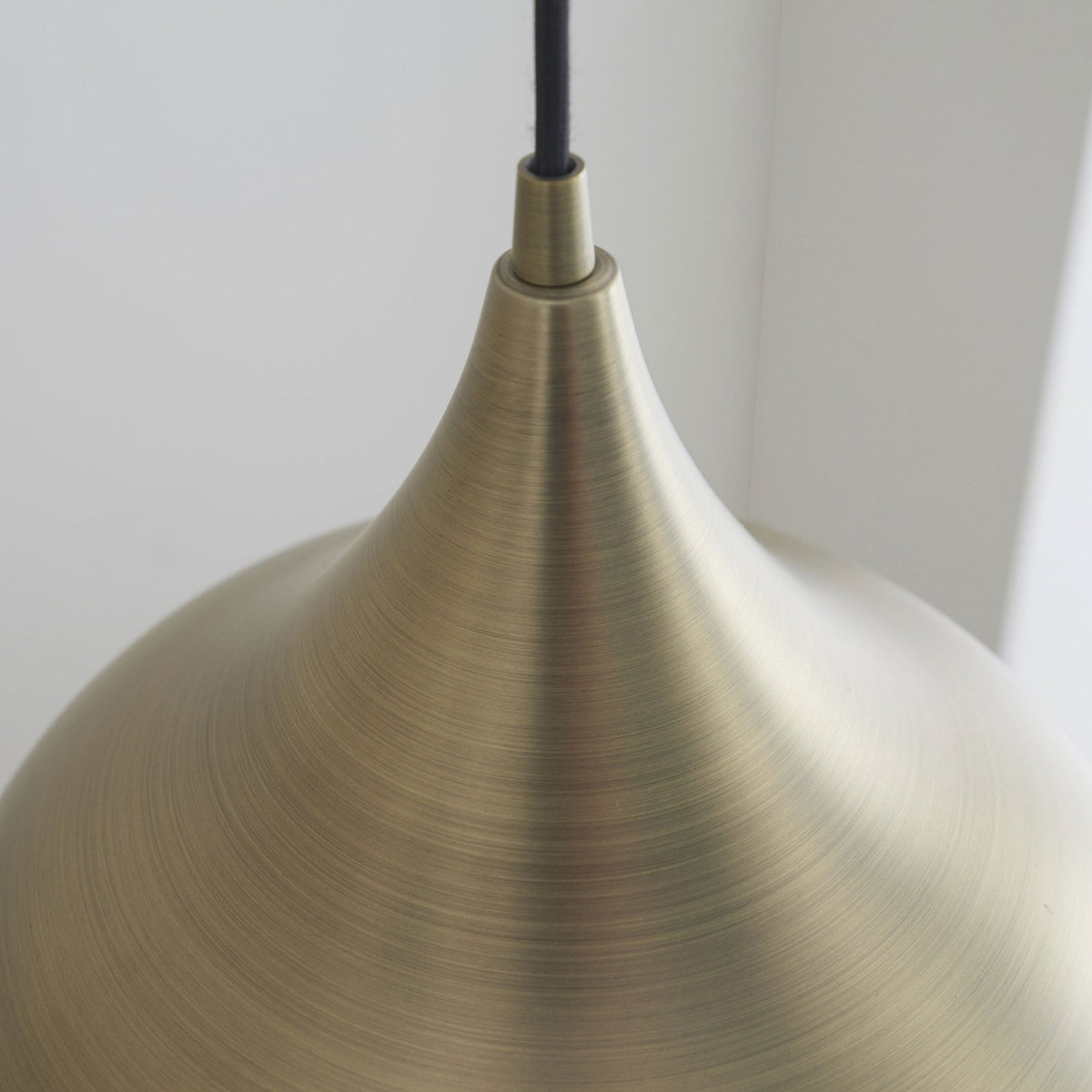 Close-up of the top portion of a brass pendant light, highlighting its smooth, curved design.
