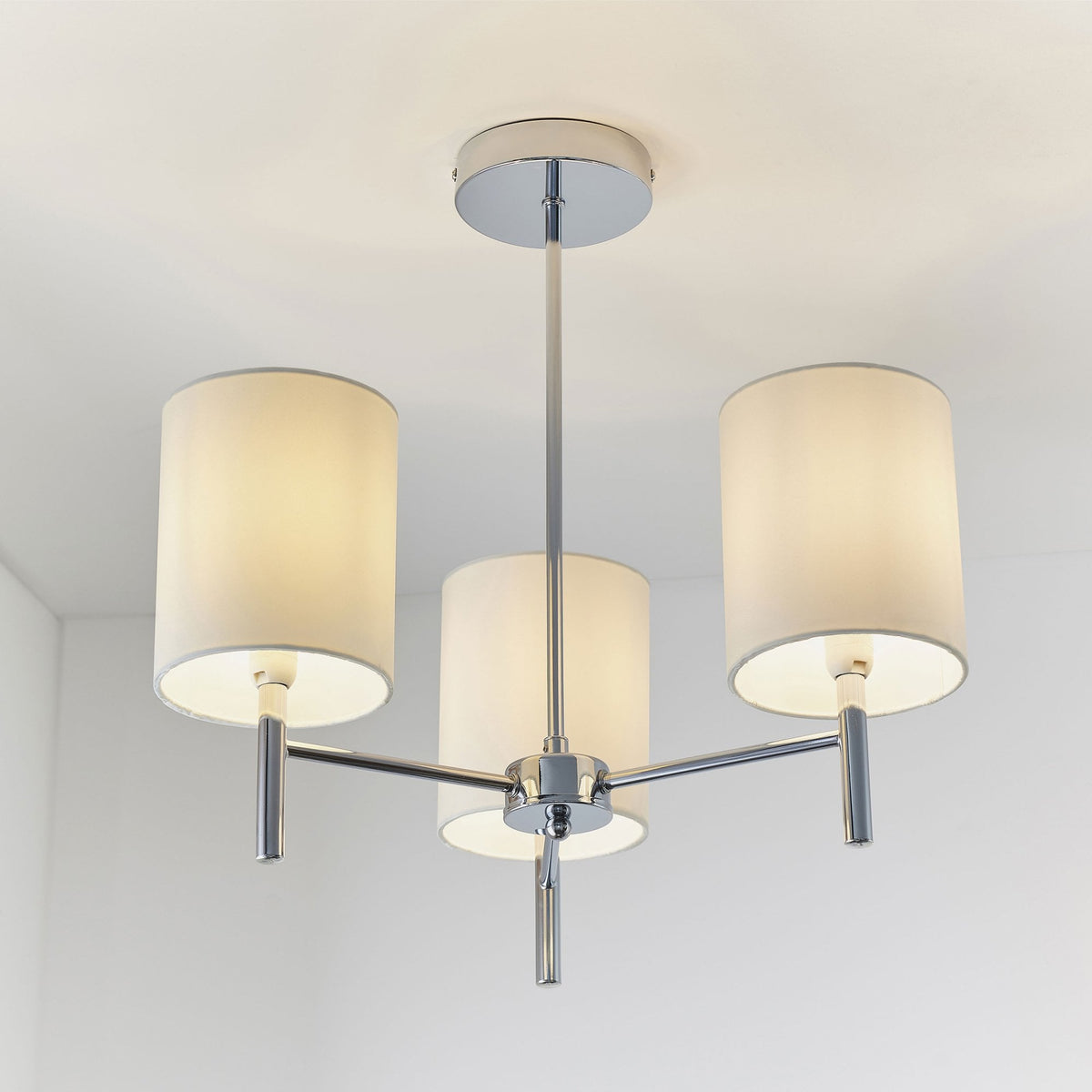 Three-light ceiling pendant with chrome finish and white fabric shades, illuminating a room.
