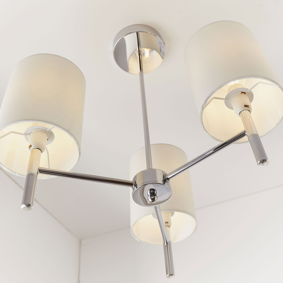 Close-up of a three-light ceiling pendant with chrome finish and white fabric shades.