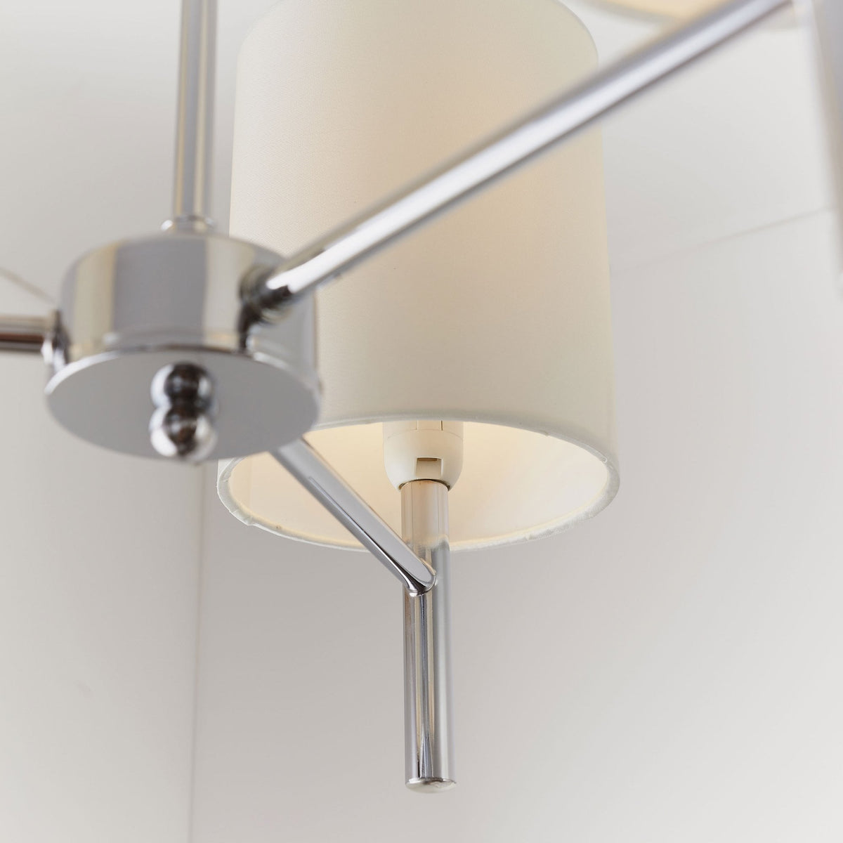Detailed view of the chrome arm and white fabric shade of a ceiling pendant.