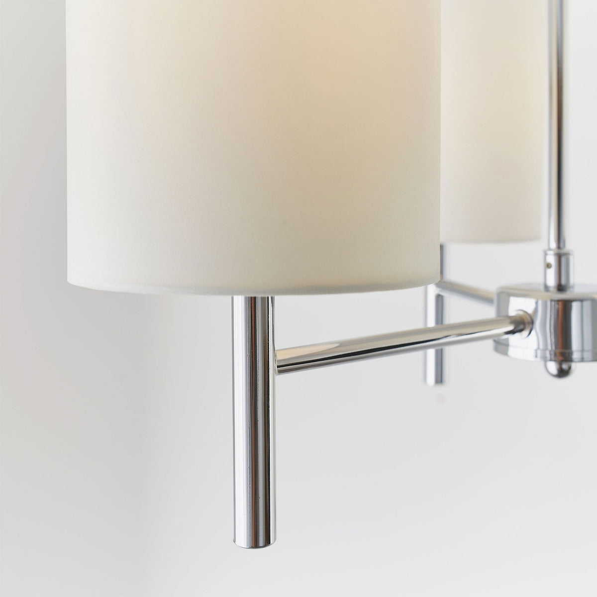 Close-up of a white fabric shade and chrome arm of a three-light ceiling pendant.