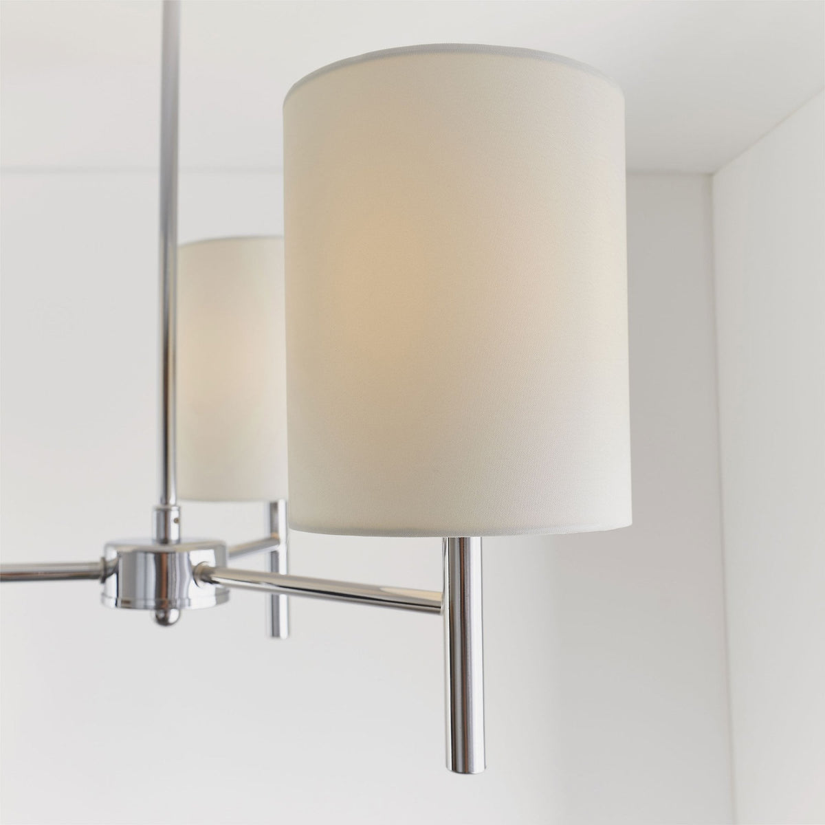 Side view of a white fabric shade and chrome arm of a three-light ceiling pendant.