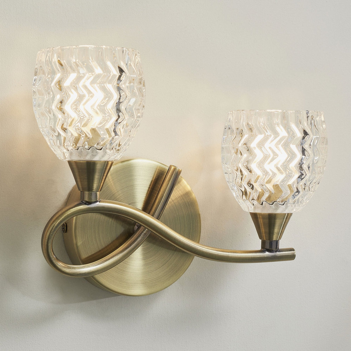 Two-light wall sconce with clear, textured glass shades and an antique brass finish.