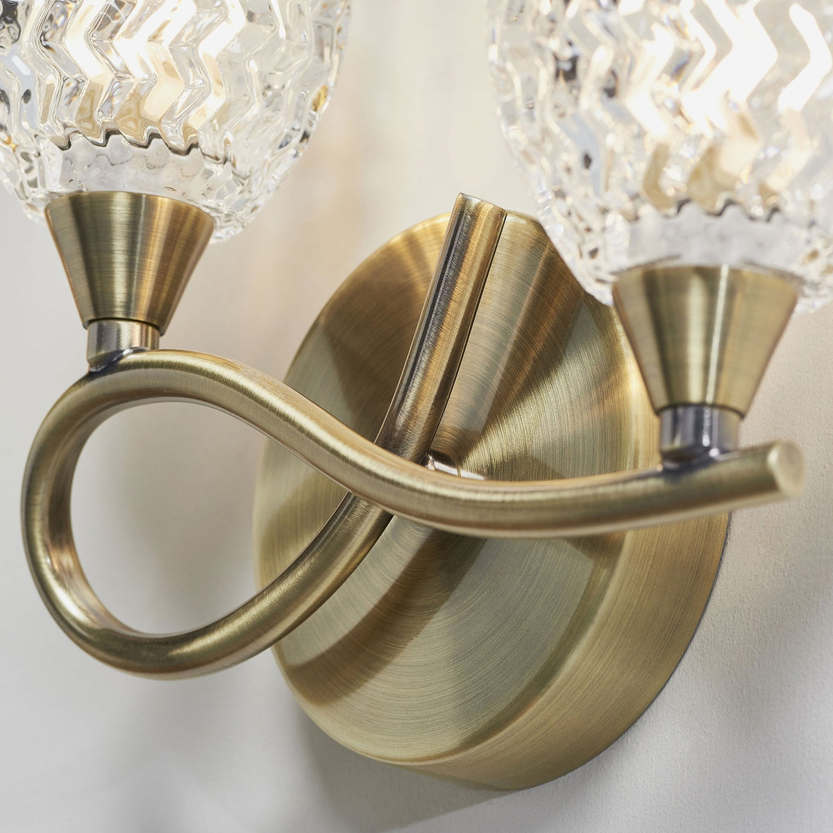 Close-up of the antique brass base and two clear, textured glass shades of a wall sconce.