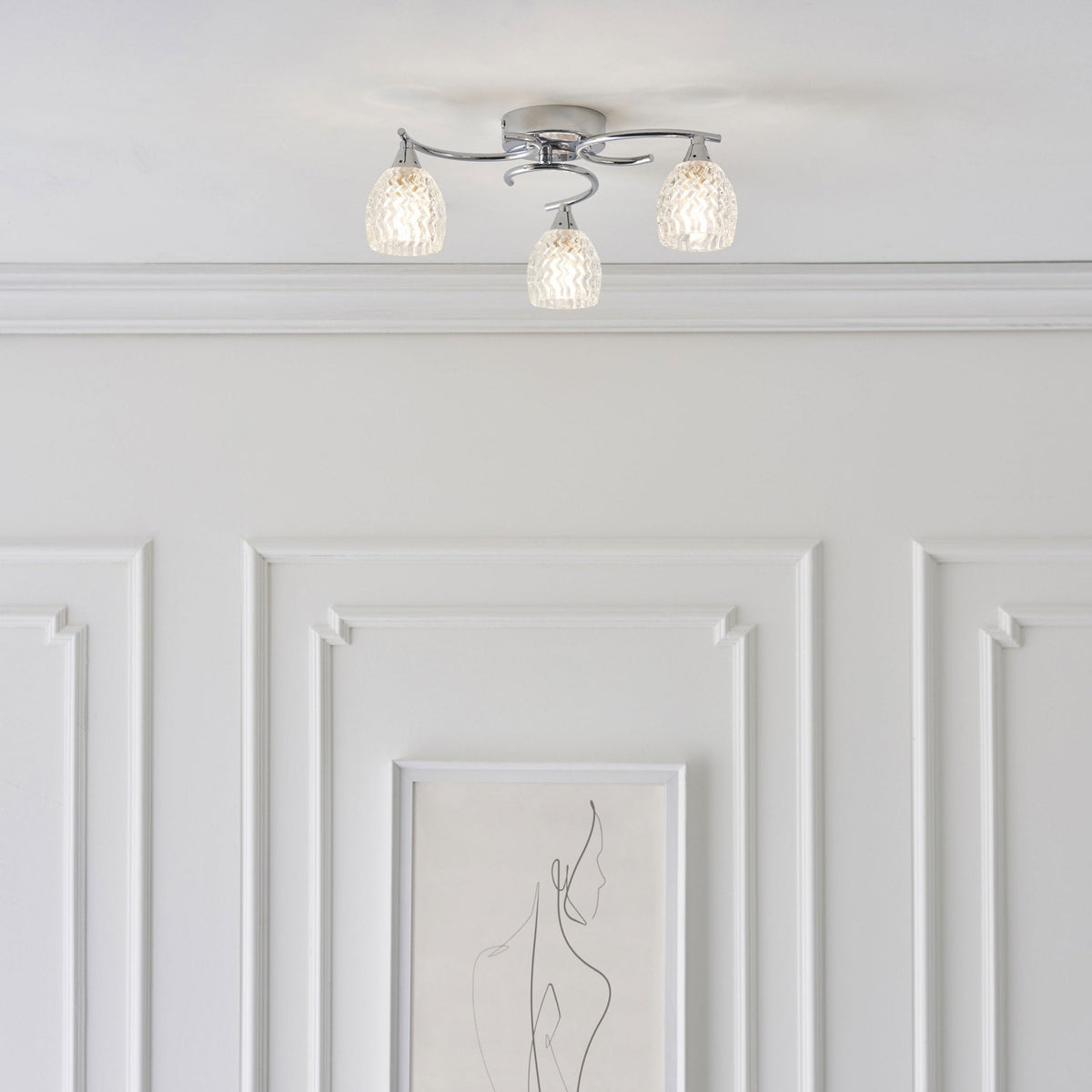 Four-light ceiling fixture with chrome arms and textured glass shades above a white paneled wall.