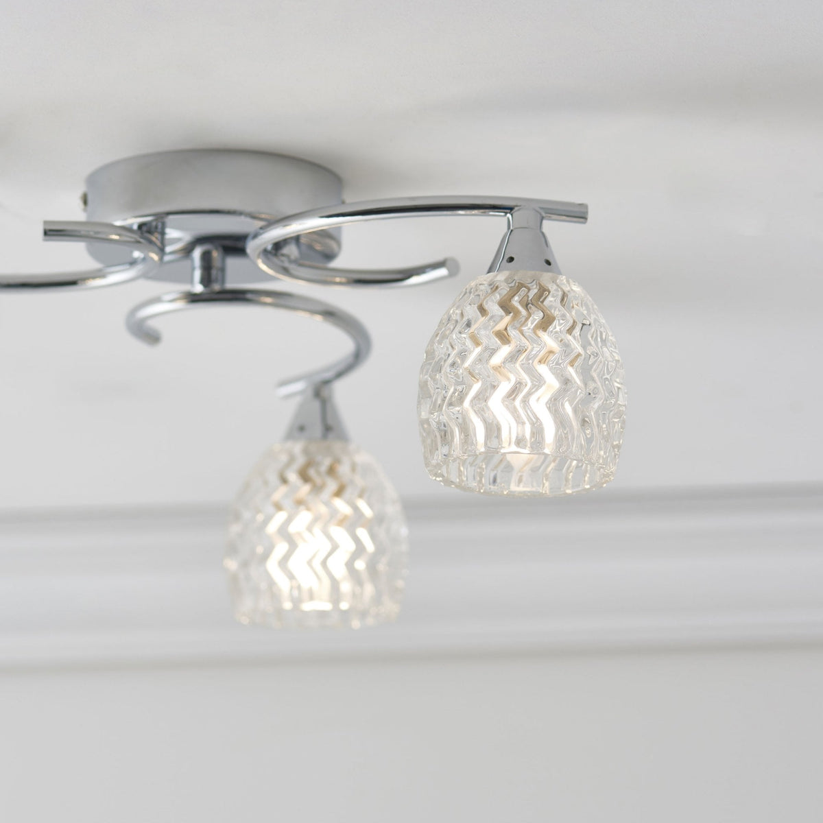 Close-up of a two-light ceiling fixture with chrome arms and textured glass shades.