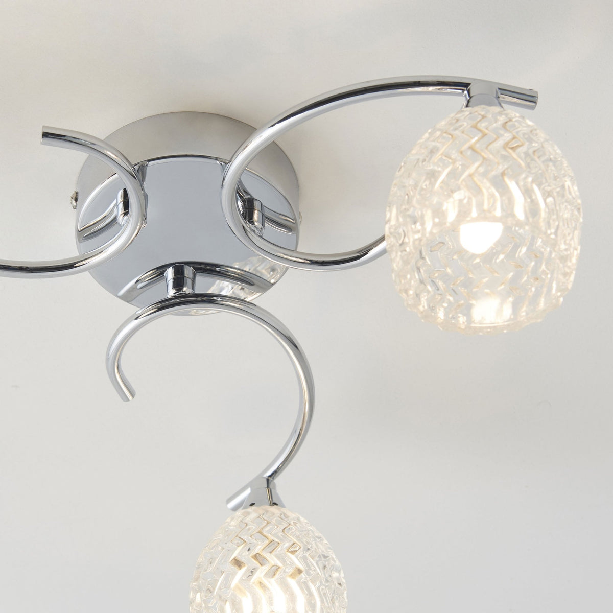 Close-up of a three-light ceiling fixture with chrome arms and textured glass shades.