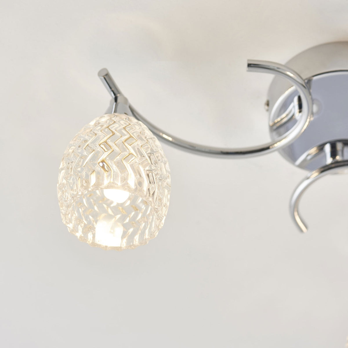 Close-up of one textured glass shade and chrome arm of a ceiling fixture.