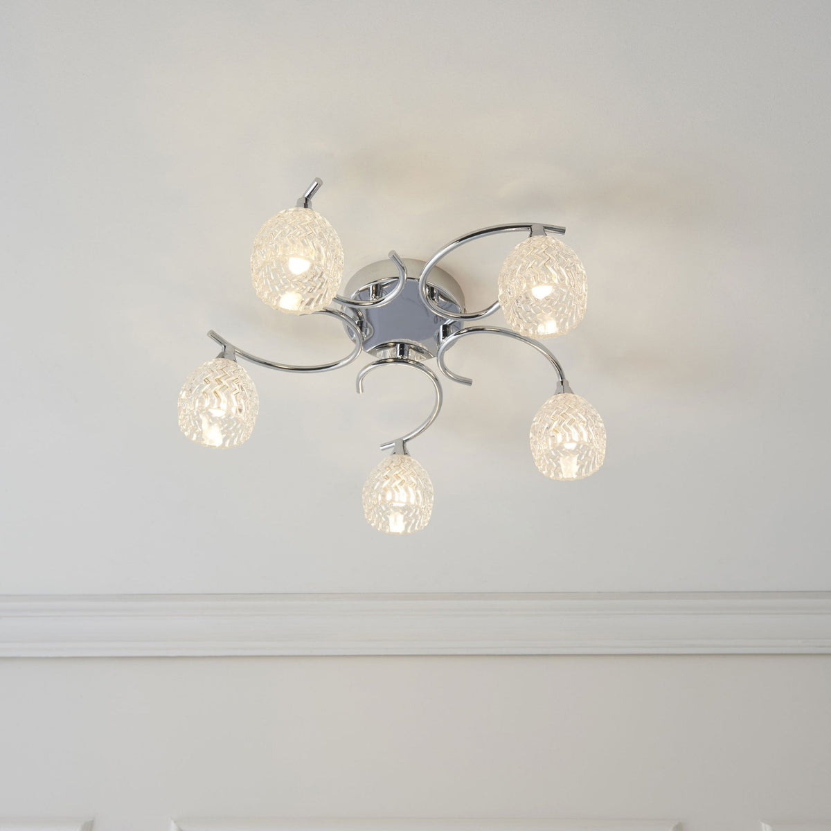 Chrome ceiling light with five clear, textured glass shades, illuminated and mounted on a white ceiling.