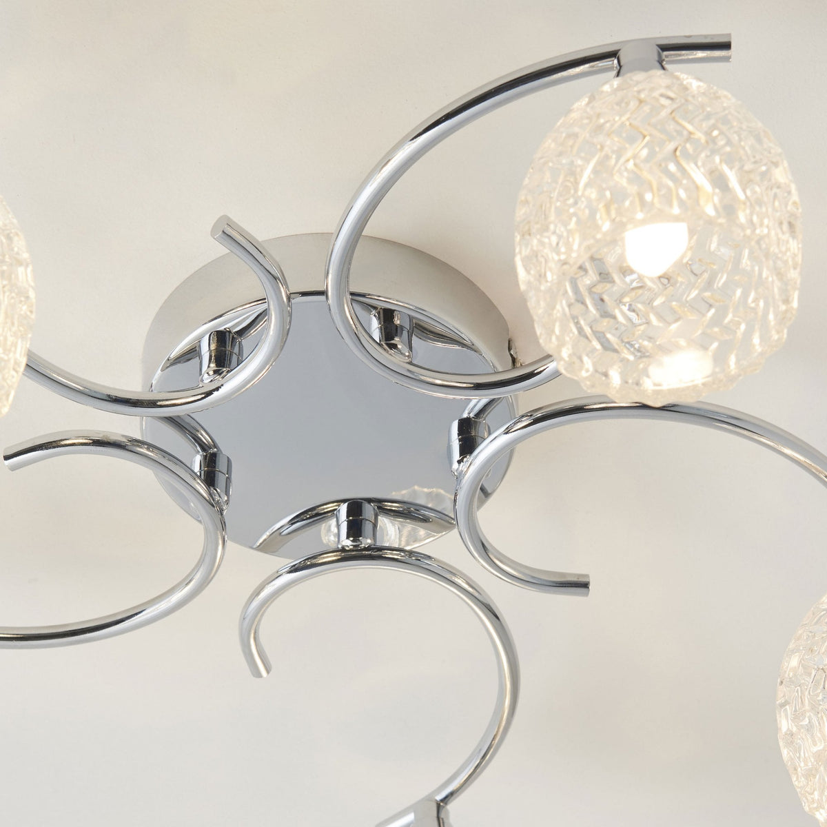 Close-up of the central chrome fixture and one illuminated, clear, textured glass shade of a ceiling light.