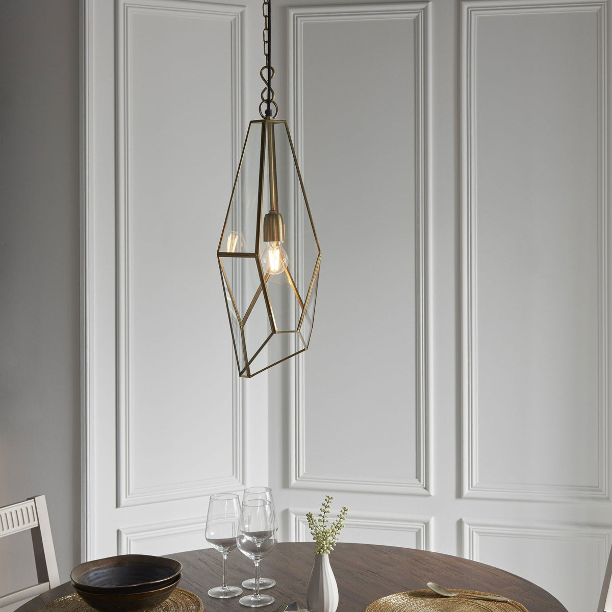 Geometric pendant light hanging above a round dining table with two chairs, glasses, and a bowl.