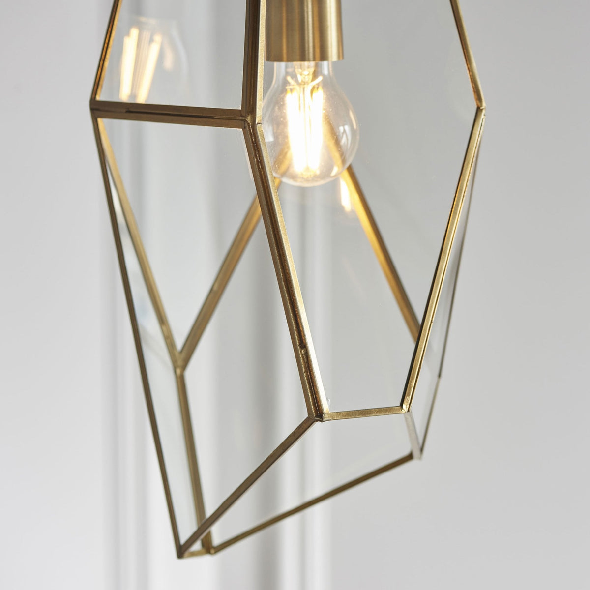 Close-up of the bottom half of a geometric pendant light, showing the brass frame and exposed bulb.