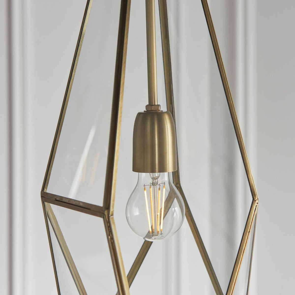 Close-up of the center of a geometric pendant light, highlighting the brass bulb holder and clear glass.