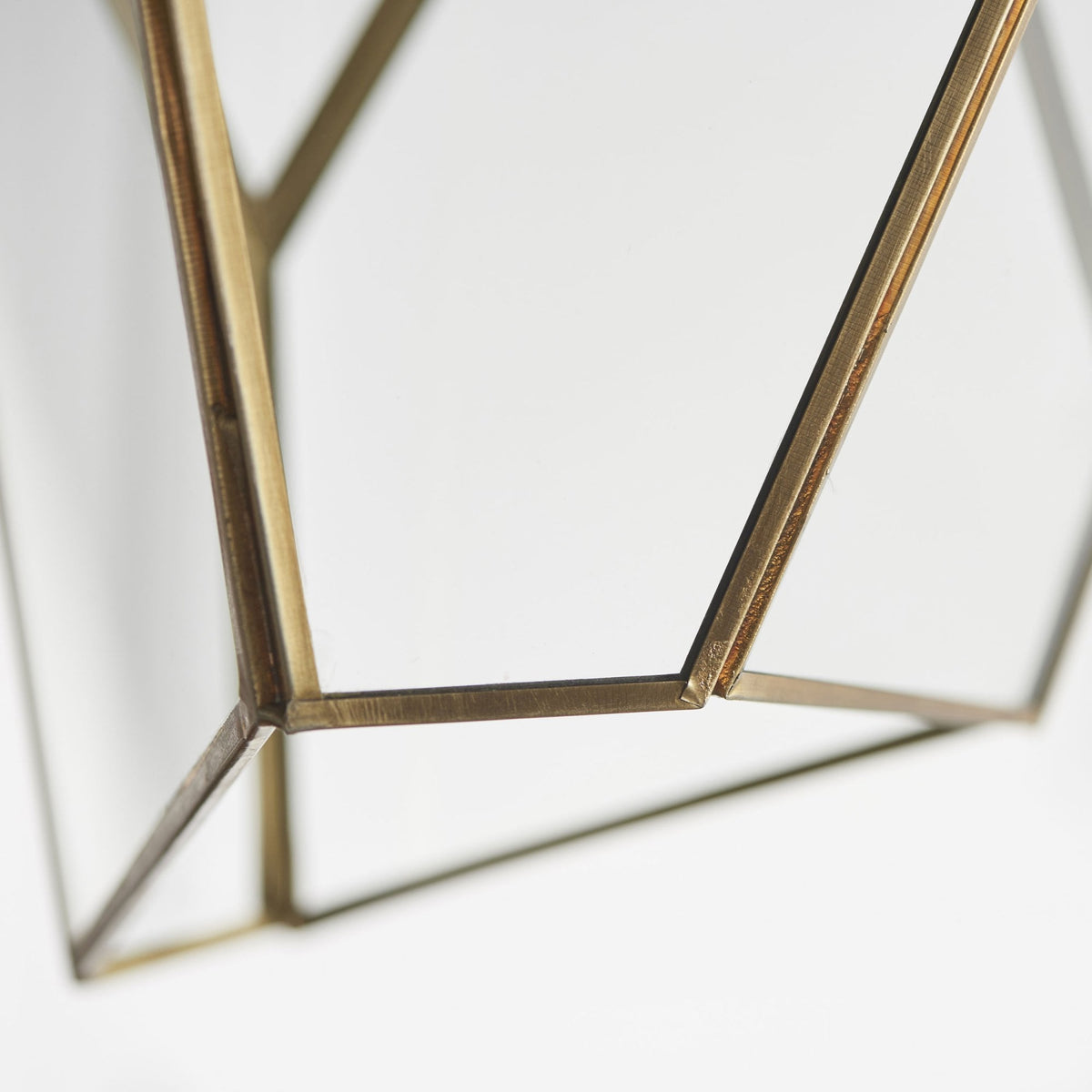 Close-up of the brass frame and clear glass panels of a geometric pendant light.