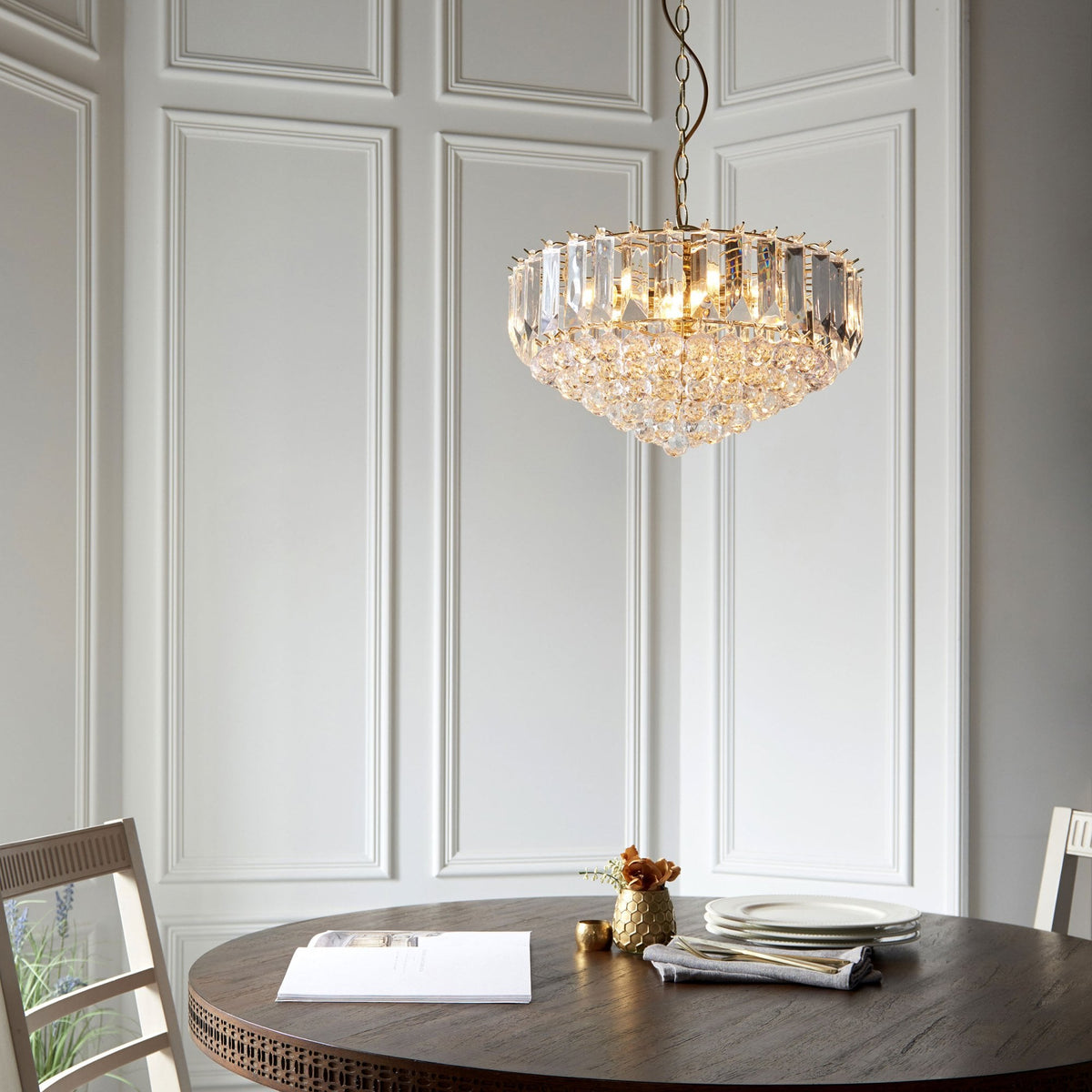 Gold and crystal chandelier hanging above a round wooden dining table with chairs.