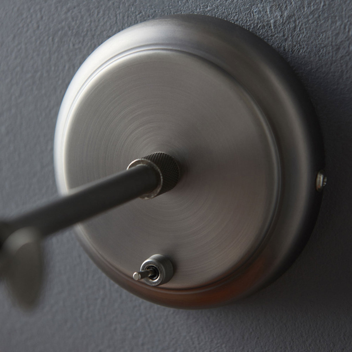 Close-up of the brushed metal wall plate of the light fixture with a small toggle switch.