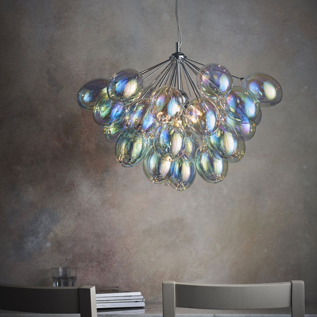 A large chandelier with iridescent glass shades hangs over a dining table with two chairs.