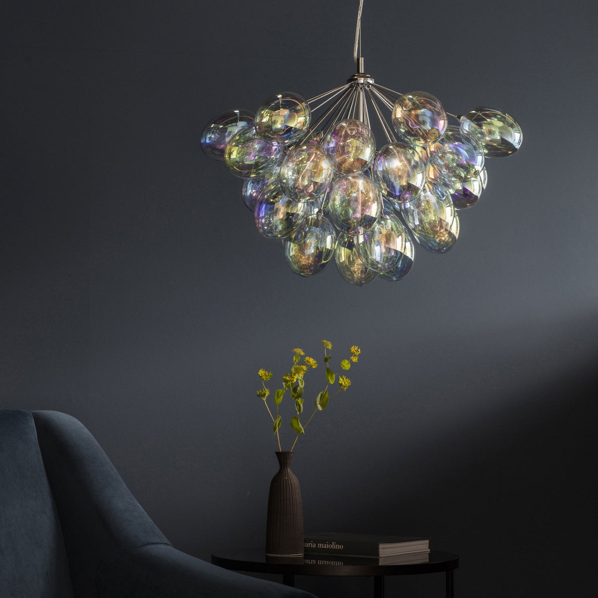 A chandelier with iridescent glass shades illuminates a modern living space with a dark blue wall.