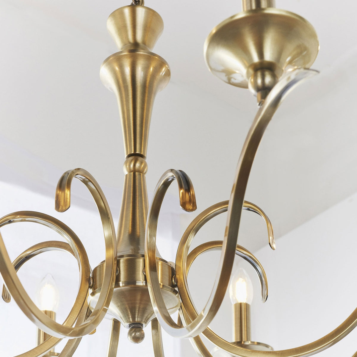 Detailed view of the antique brass chandelier's central column and elegantly curved arms.