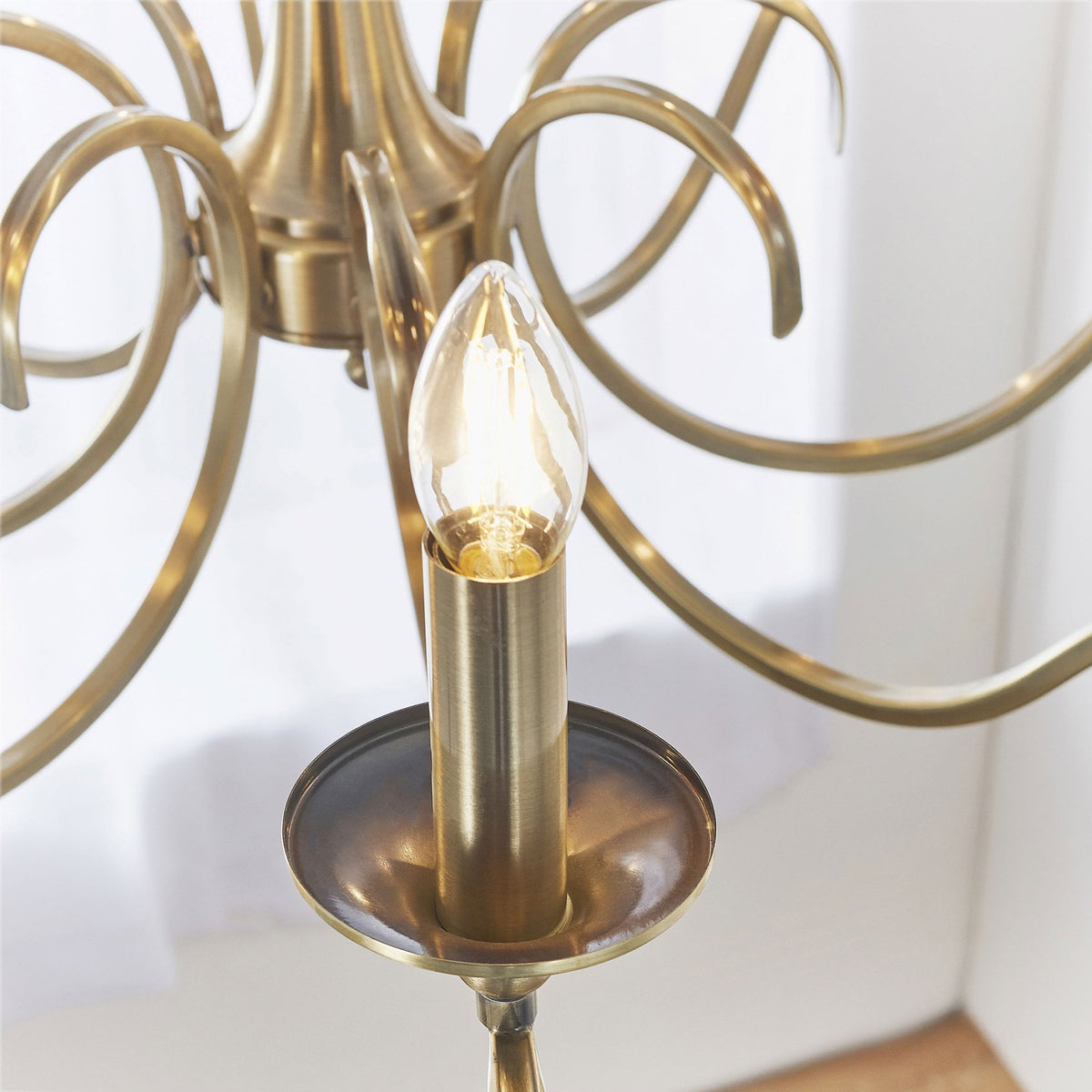 Close-up of a single lit candle-style bulb and brass holder on the antique brass chandelier.