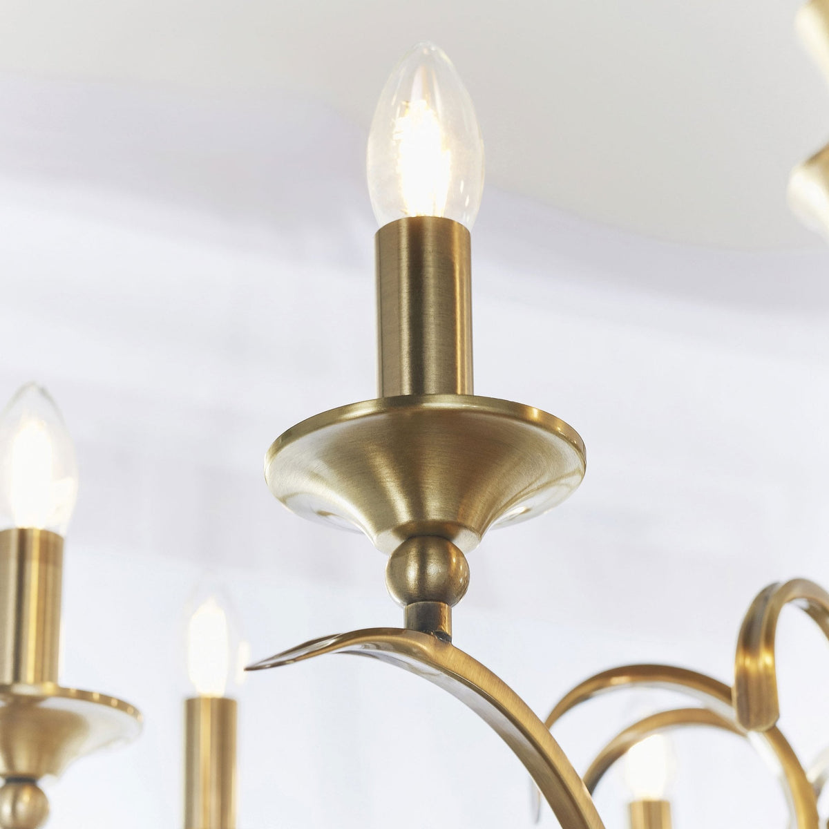 Close-up of a lit candle-style bulb and brass cup on the antique brass chandelier.