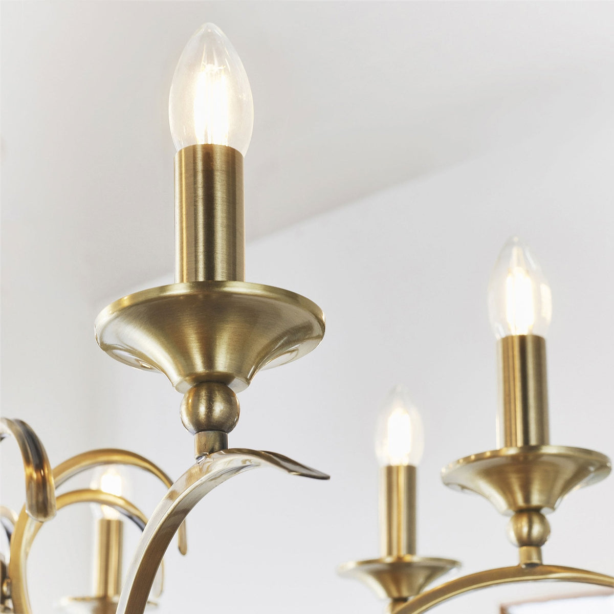 Close-up of two lit candle-style bulbs and brass holders on the antique brass chandelier.