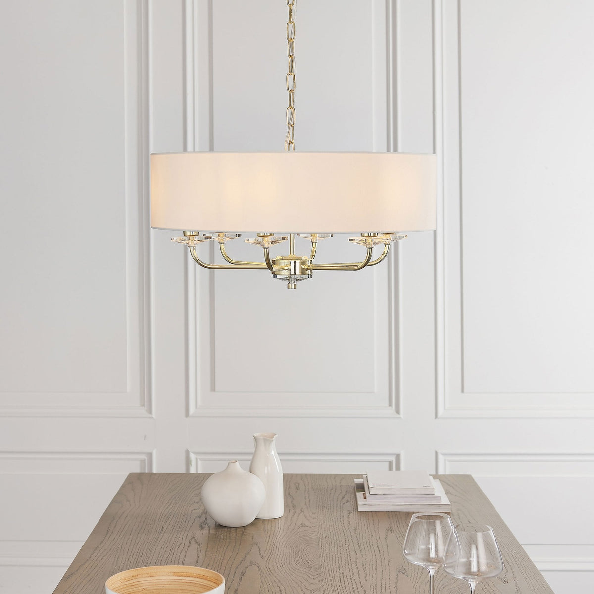 Drum shade chandelier with gold accents and crystal details hanging over a dining table.
