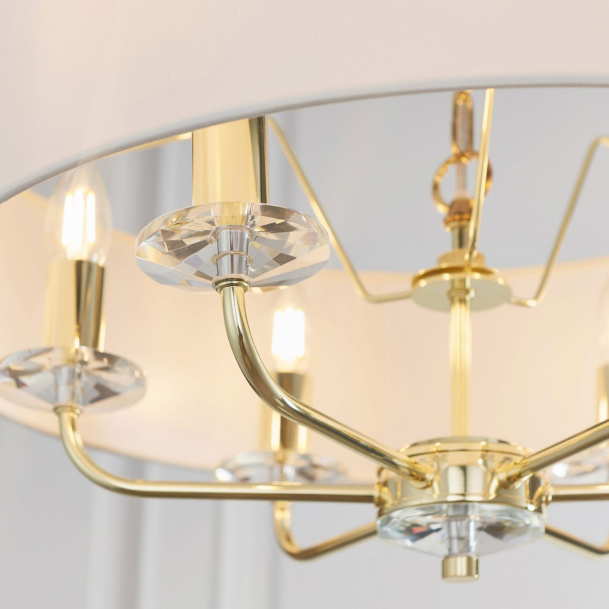 Close-up of the chandelier's gold arms, crystal accents, and exposed bulbs under the drum shade.
