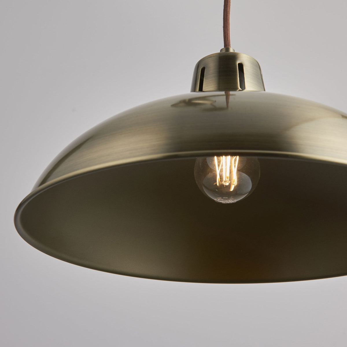 Close-up of the brass dome shade of a pulley pendant light, showing the exposed bulb.