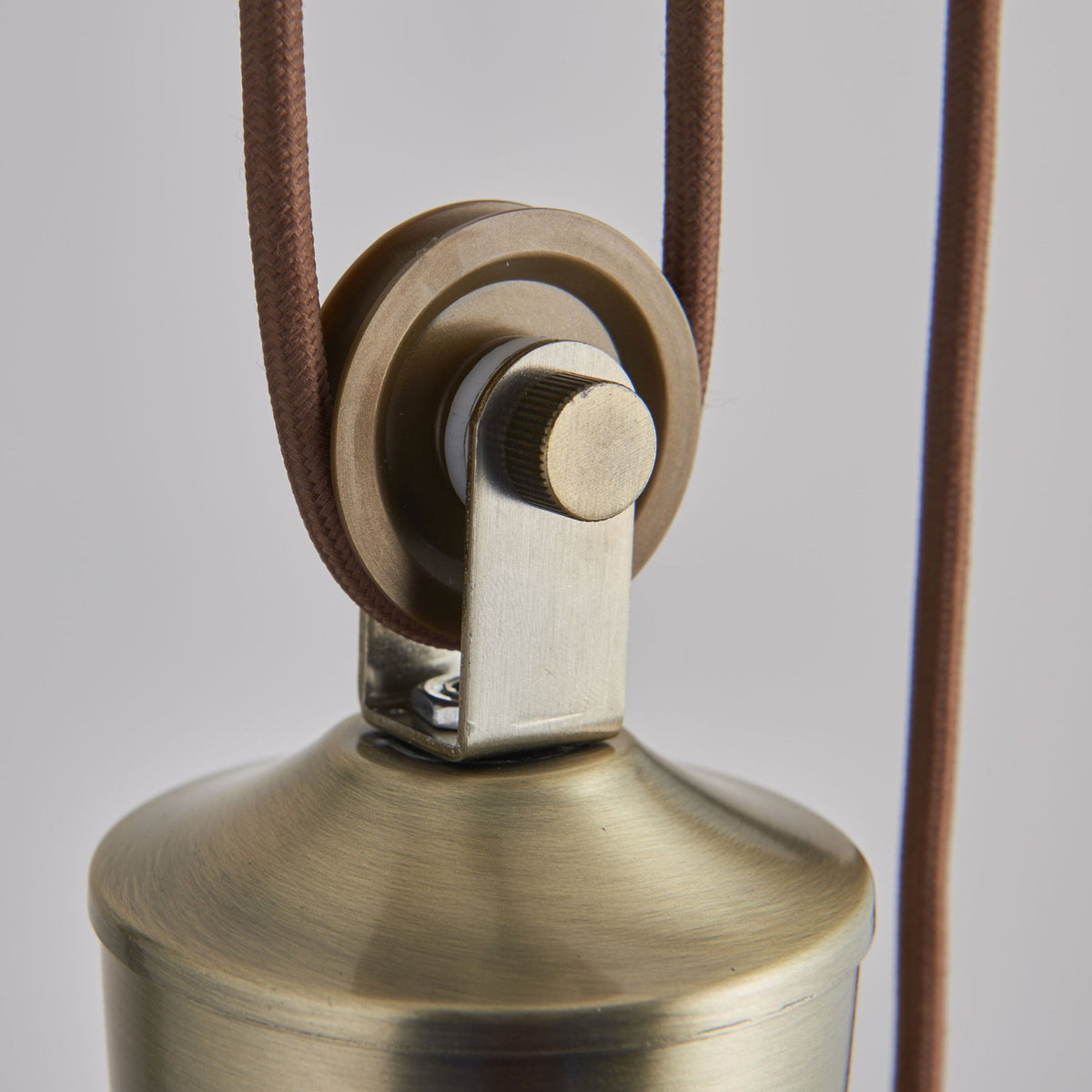 Close-up of the brass pulley mechanism on a pendant light with a brown braided cord.