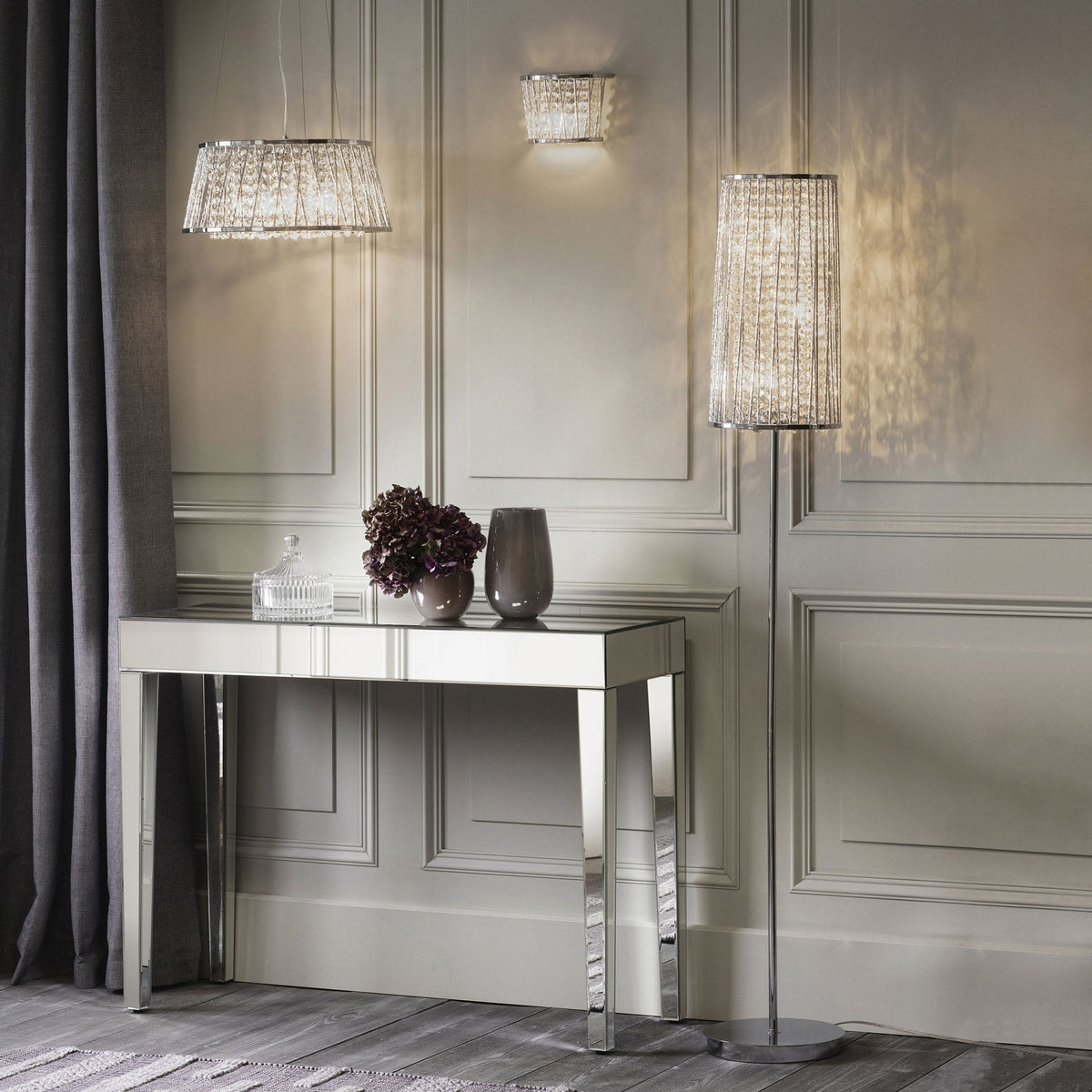 A room with a mirrored console table, a crystal chandelier, a matching floor lamp, and a wall sconce.