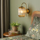 A bedroom with a green wall, a rattan headboard, and a floral duvet cover. A plant sits on a wooden nightstand.
